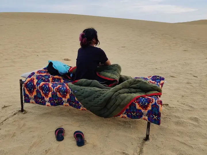 A camp bed made up with quilts on the open dunes, nothing overhead