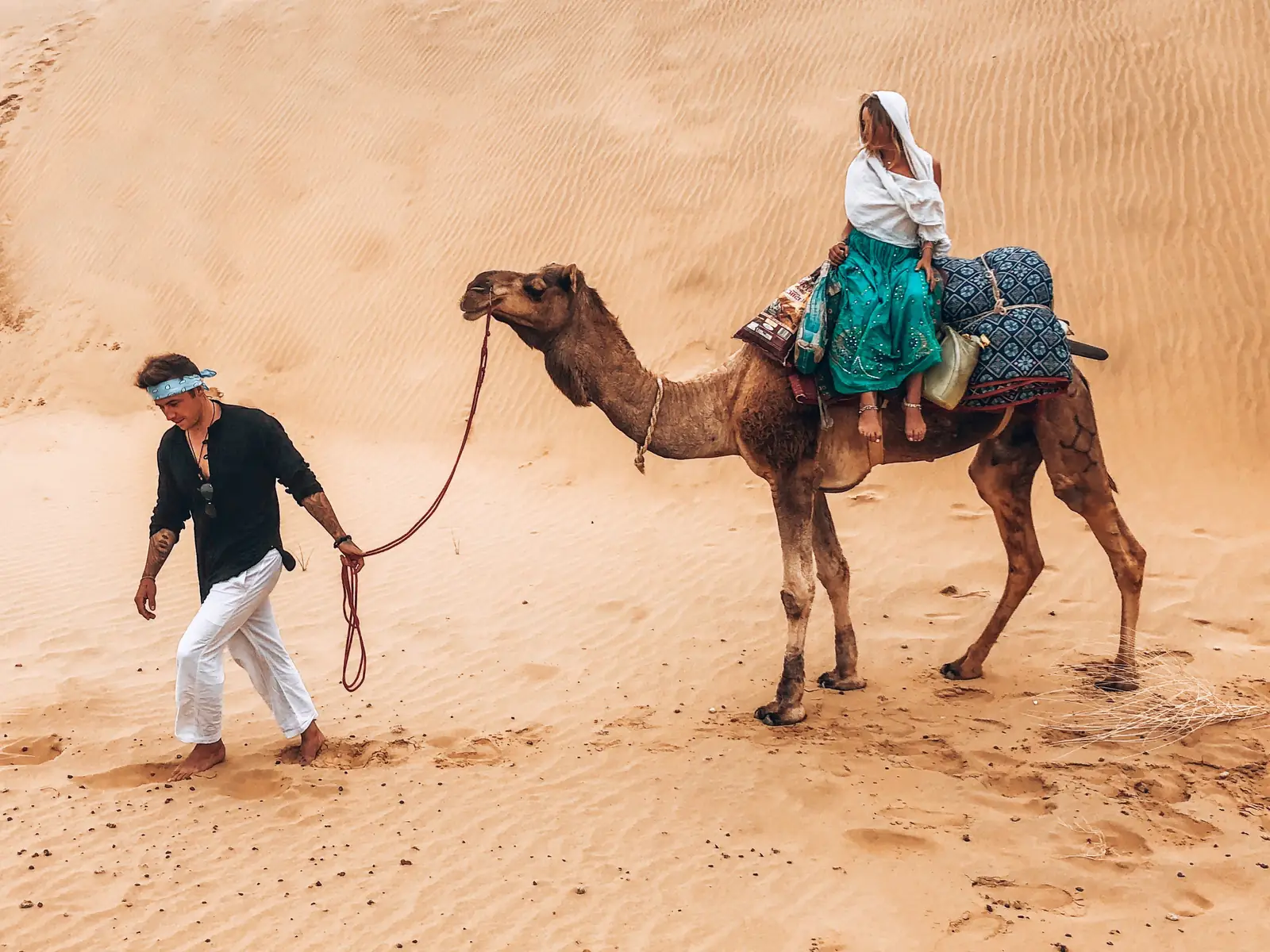 A cameleer leading a camel and its rider along the crest of a dune