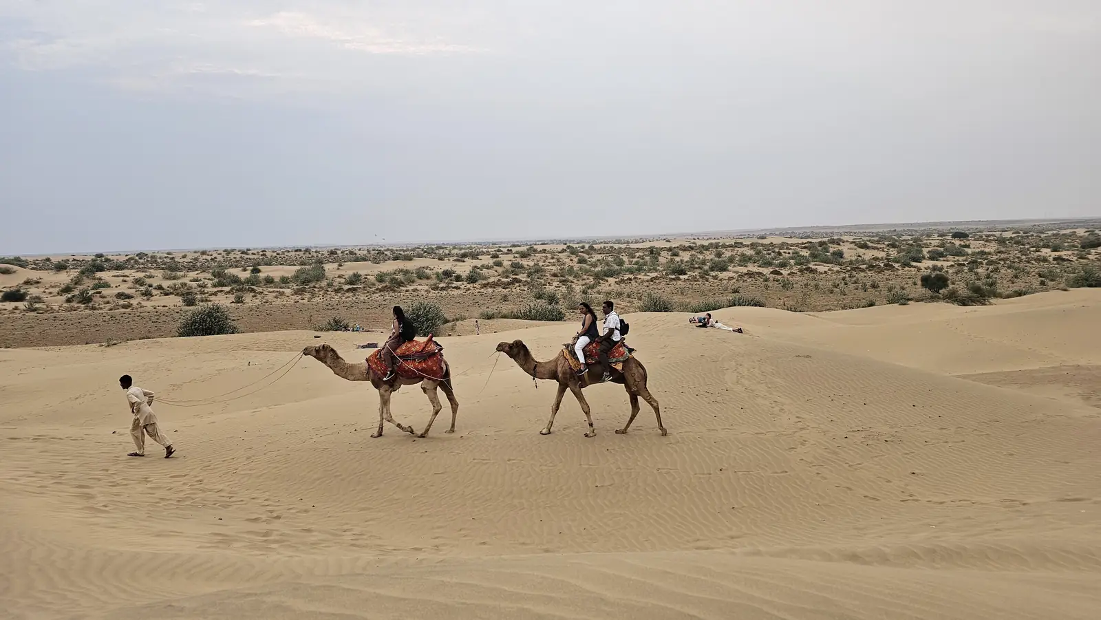 Two camels and their riders small against a wide sweep of sand