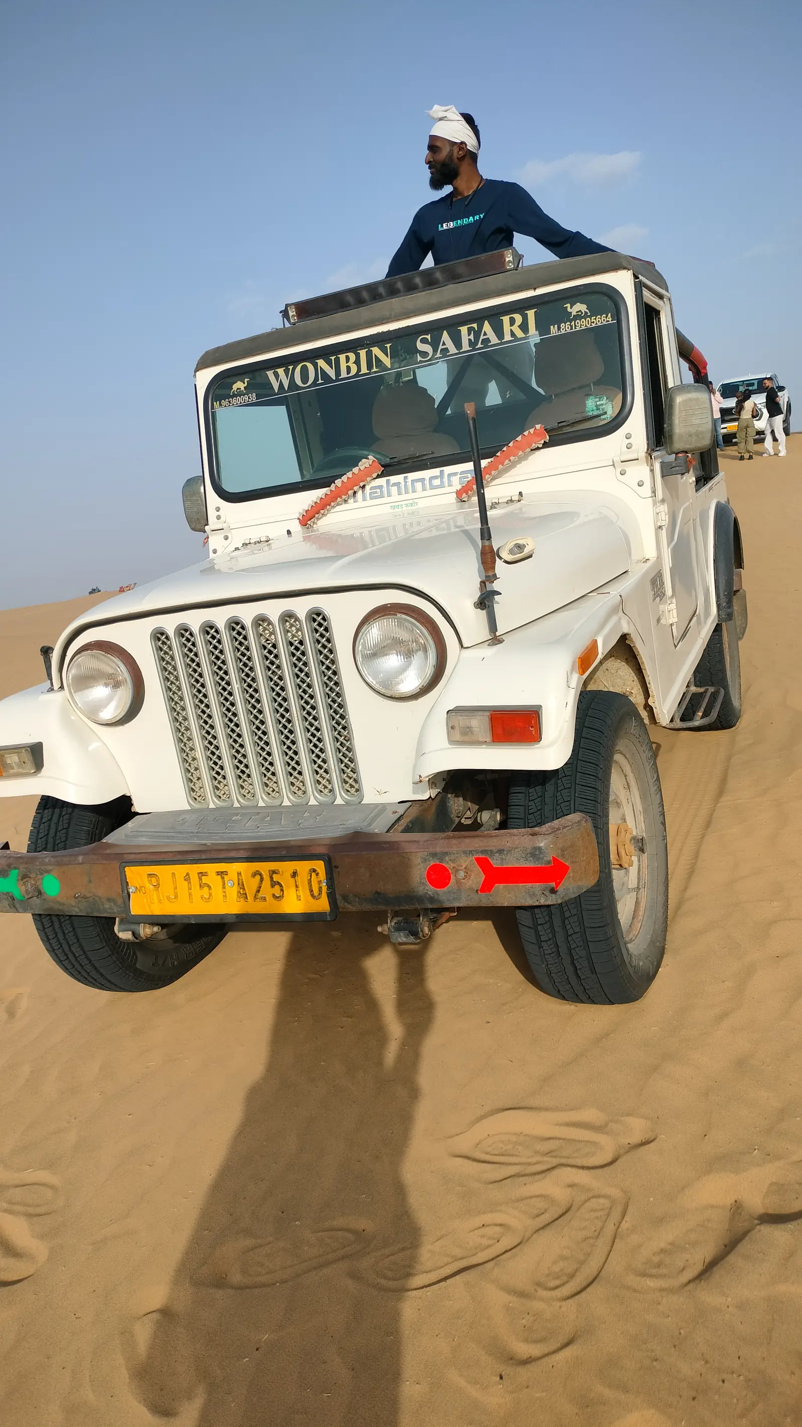 A guide sitting up on the roof of the jeep out on the dunes
