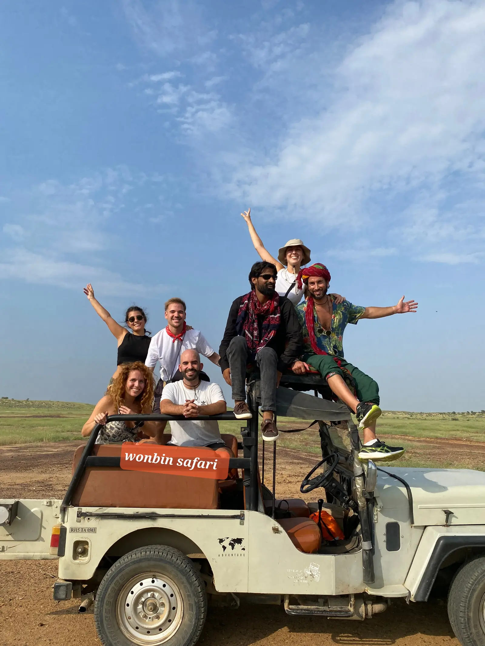 Guests riding out on the roof of the jeep, arms up, under a wide blue sky
