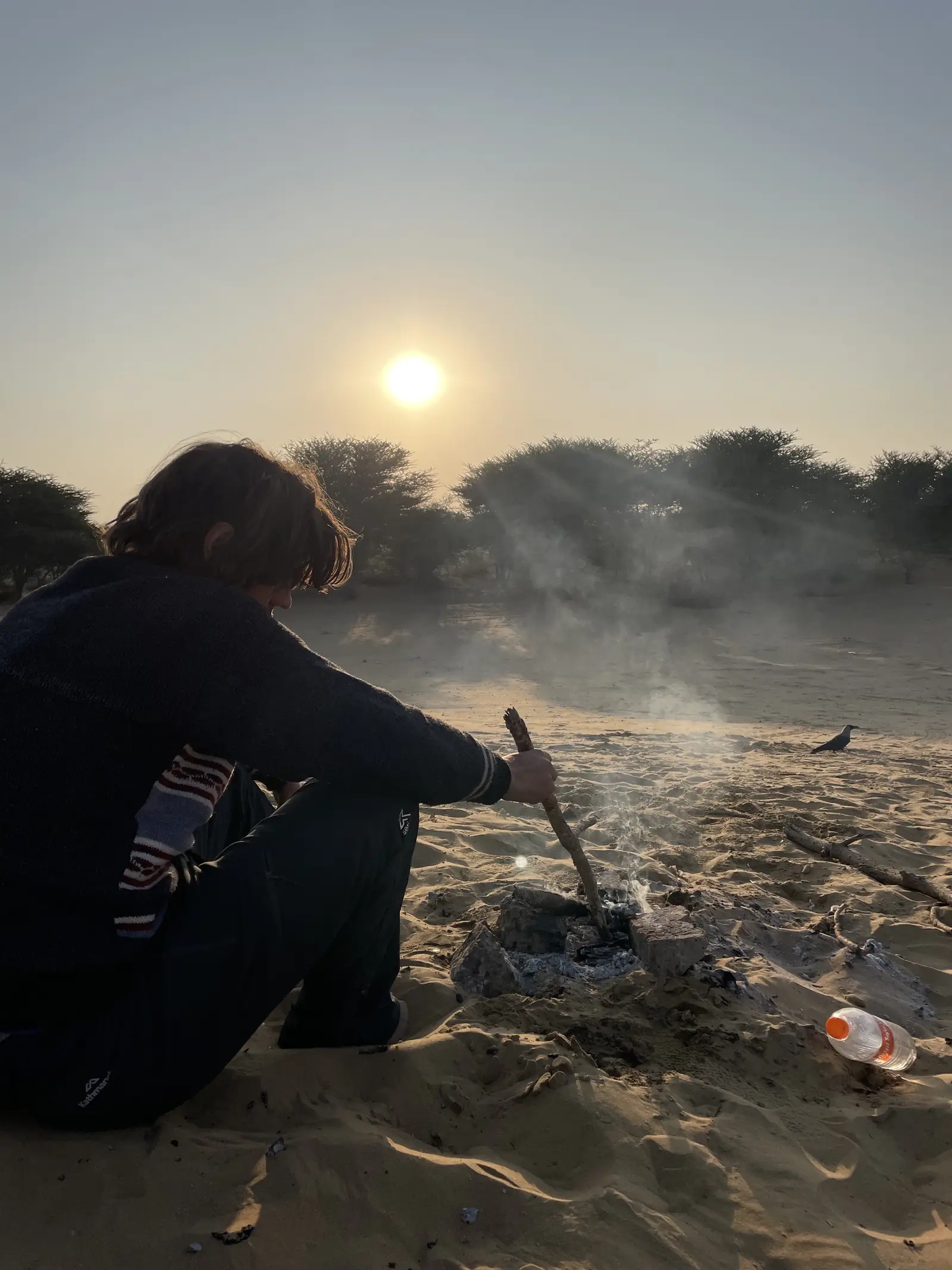 A guest crouched at the fire on the sand with the moon up