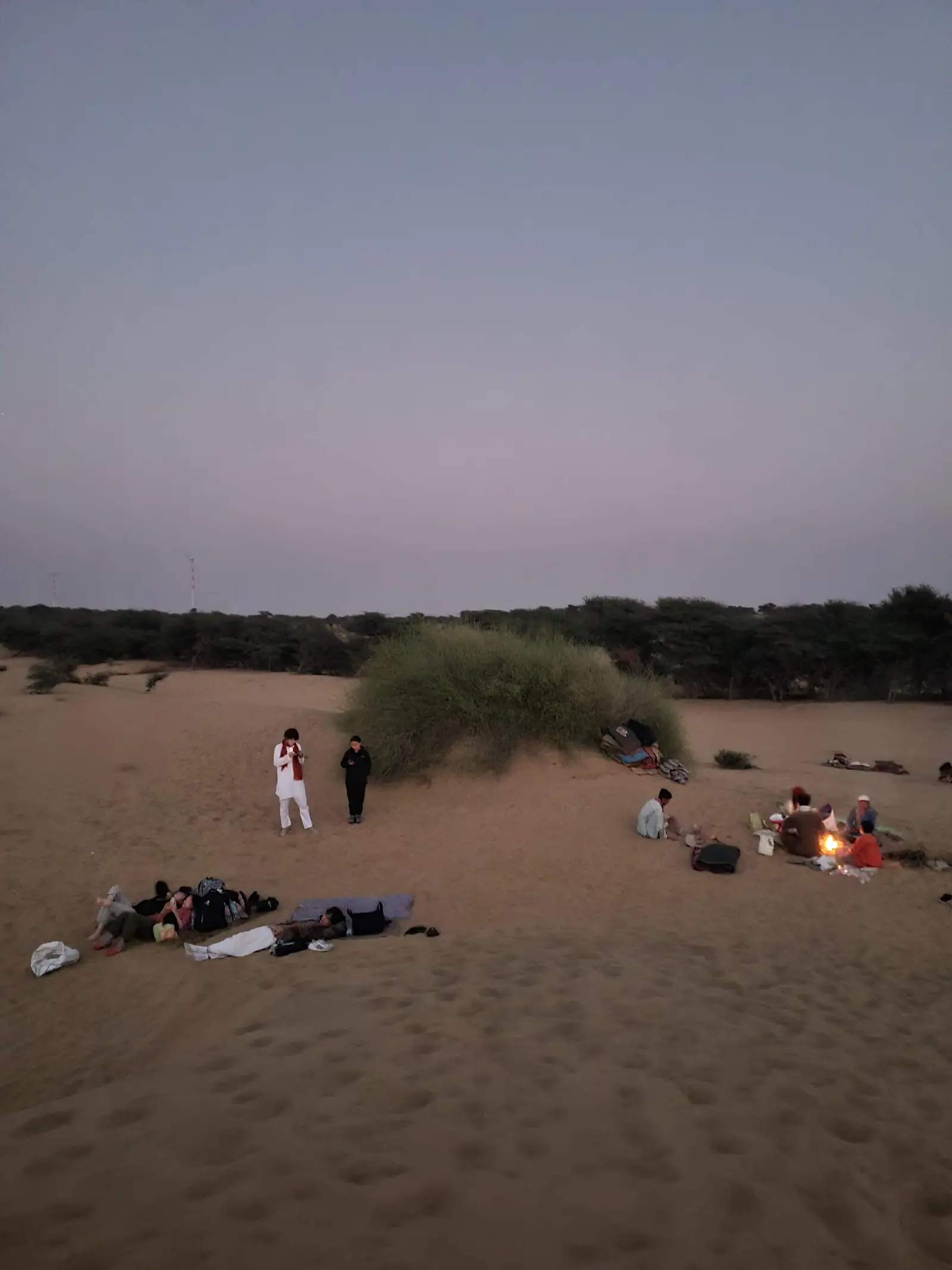 Guests gathered at a small fire in the dark, the dunes behind