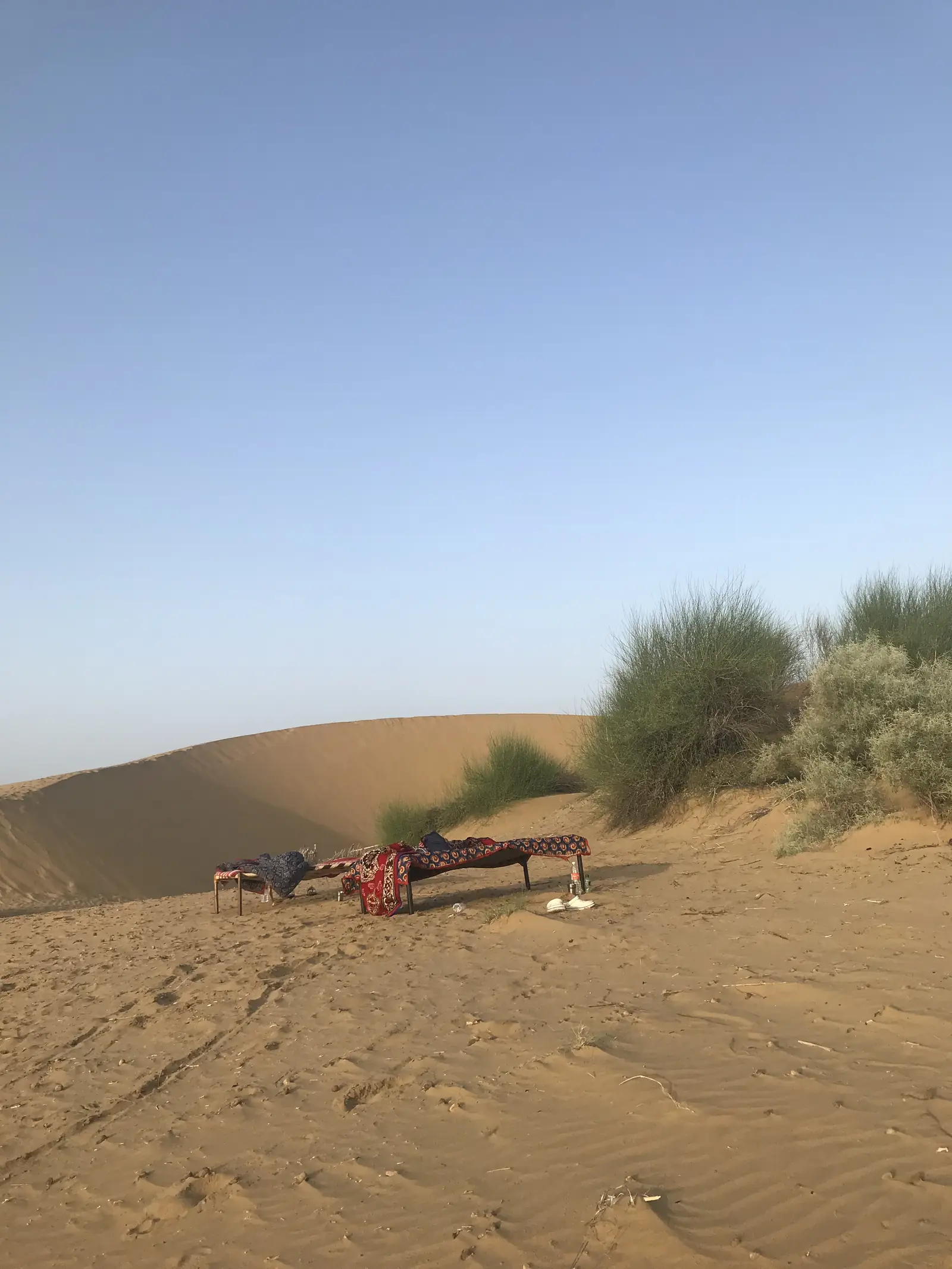 A bed made up alone on the dunes with the camp behind