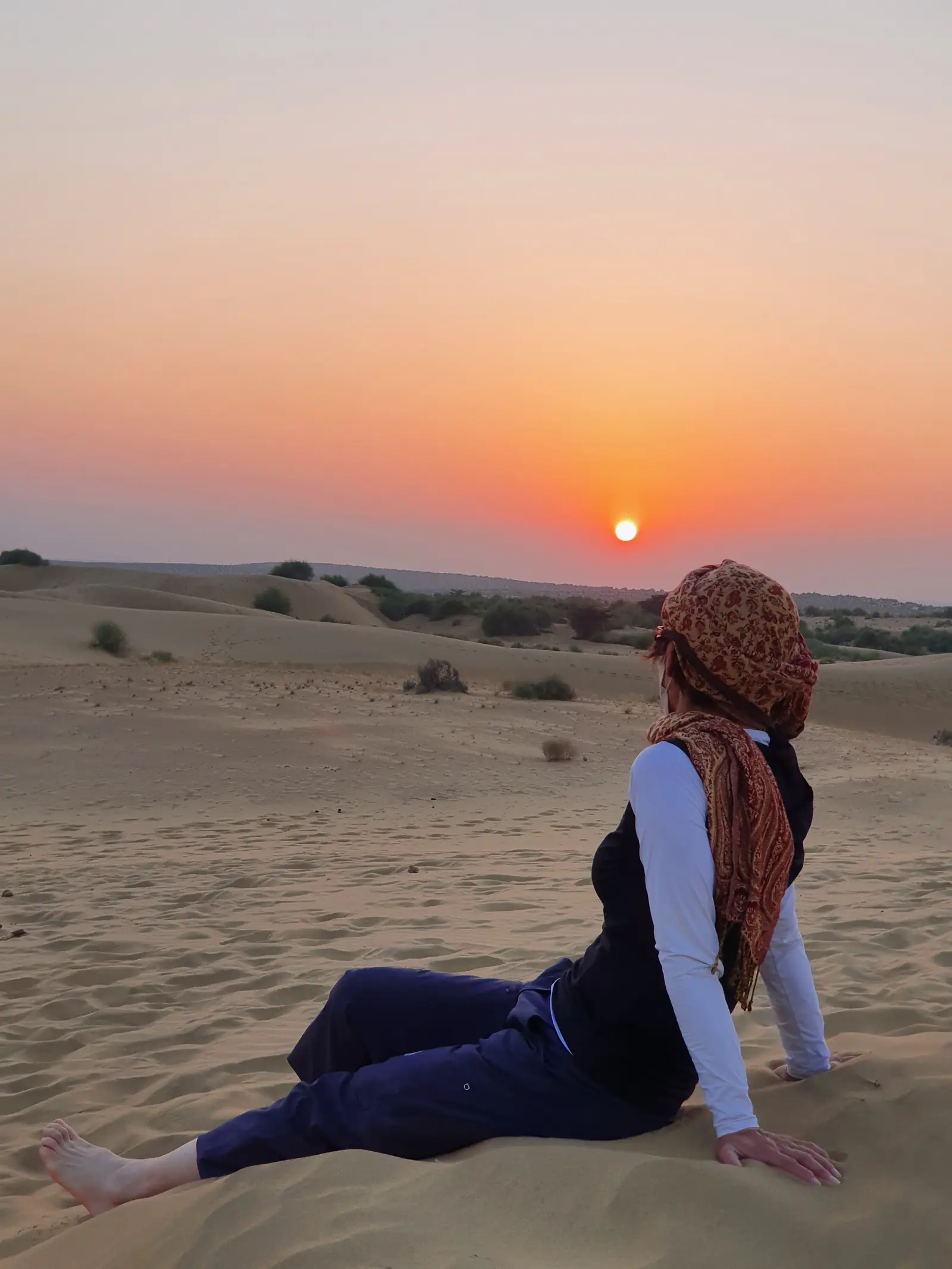 A guest sitting on the sand watching the sun go down