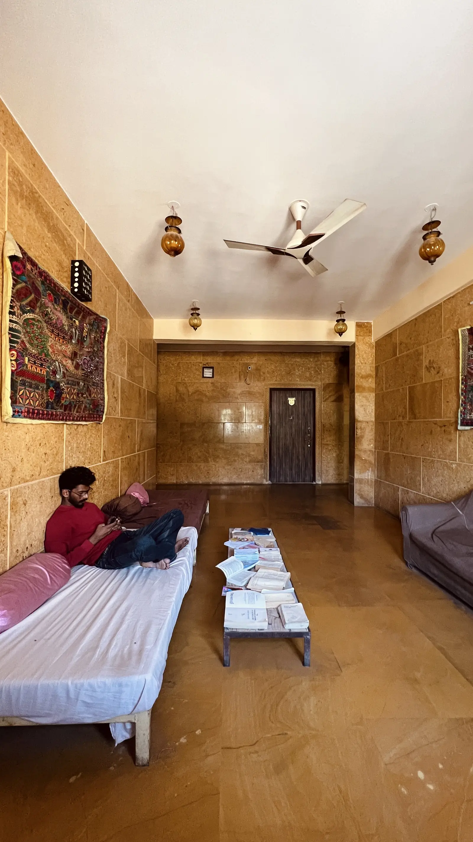 A room with a bed and a fan, sandstone walls
