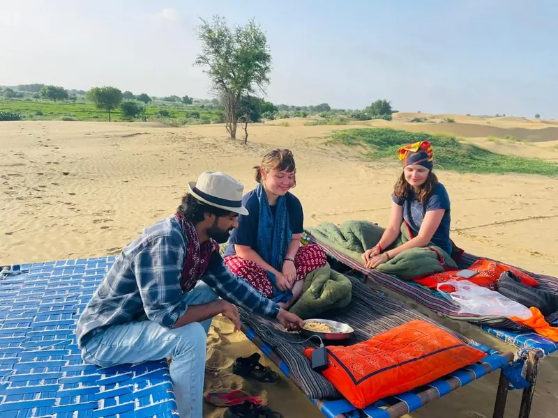 A guide serving lunch to guests on a charpoy out in the open desert