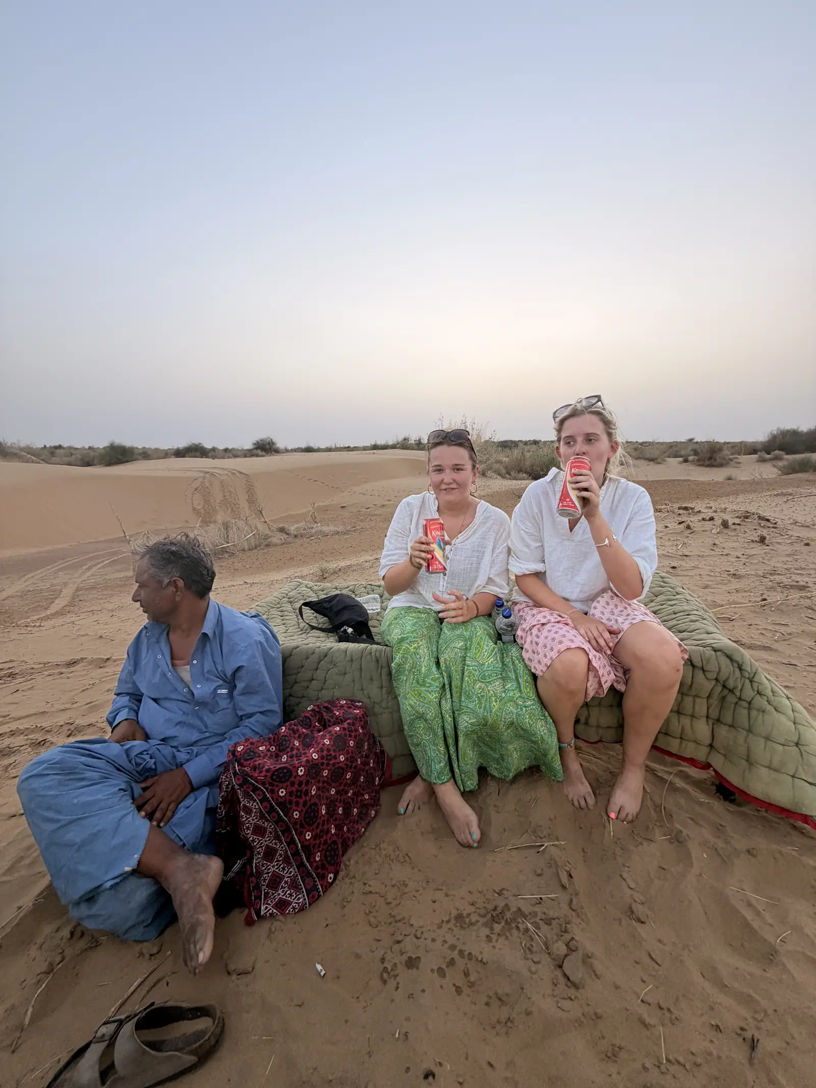 Bedding laid out on the open sand in daylight, with a crew member and two guests