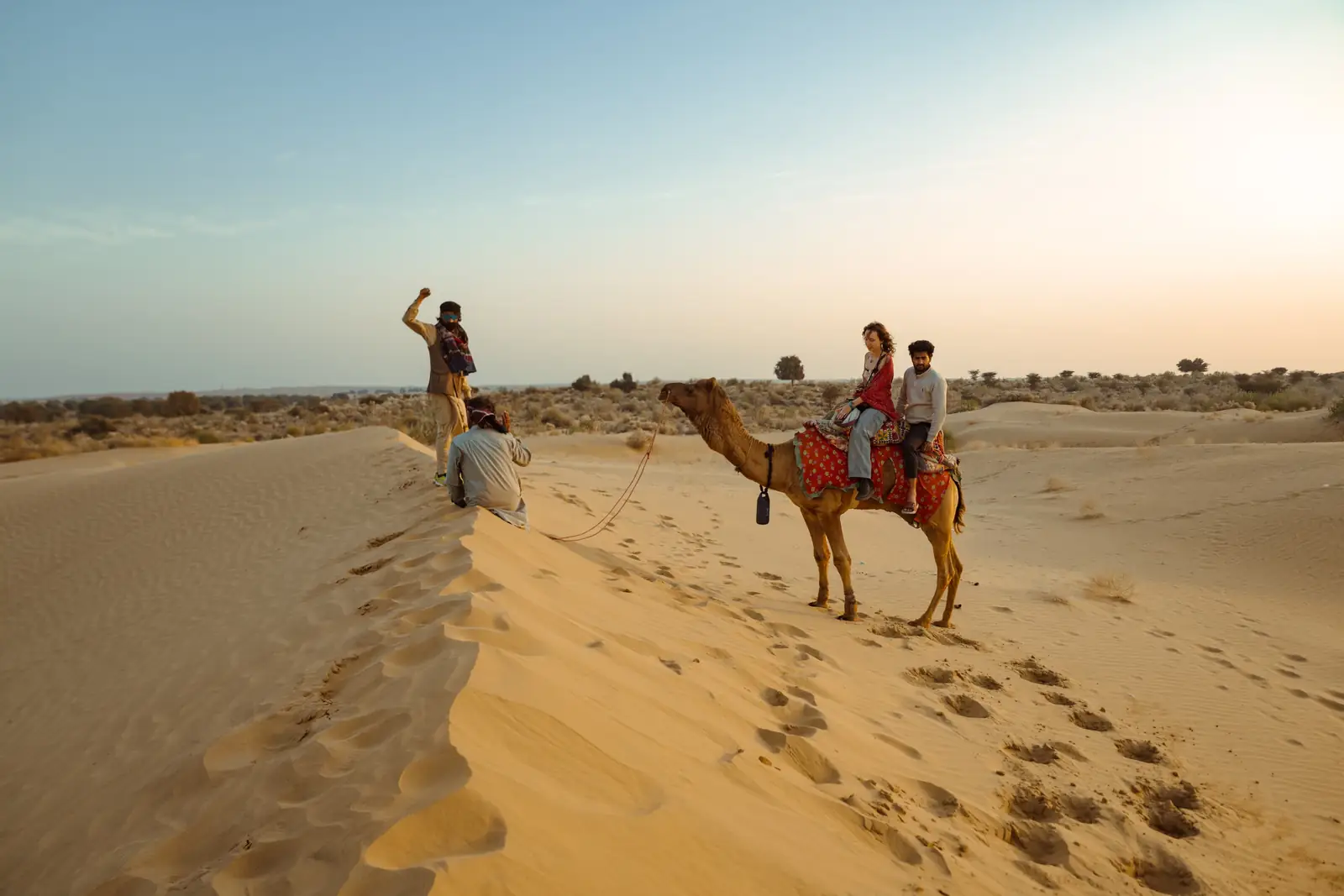 Guests riding camels up the face of a dune in the afternoon