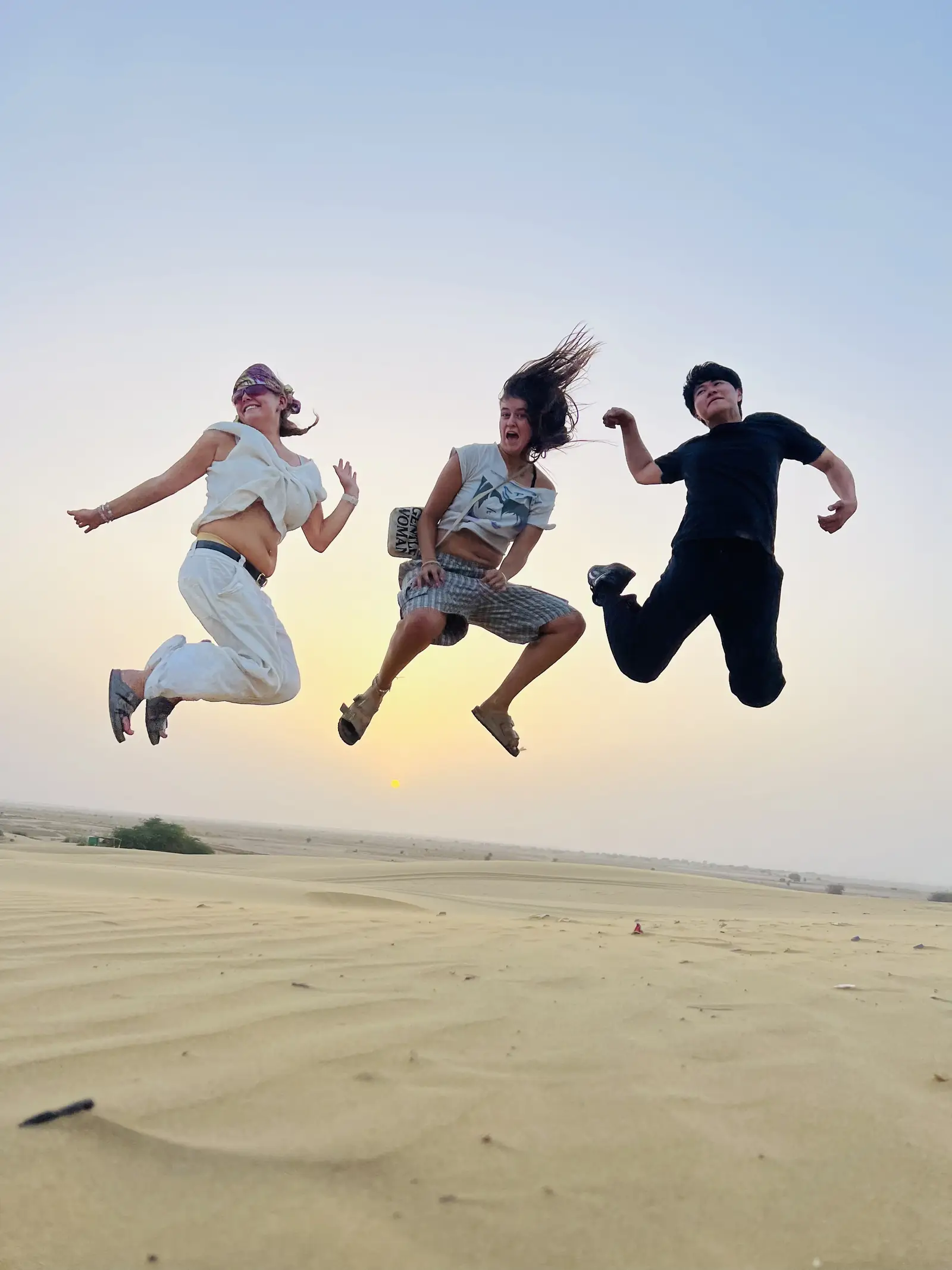 Three guests mid-jump on the crest of a dune under a clear sky