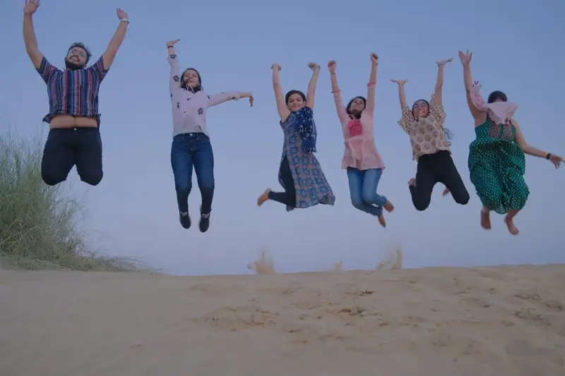 Six guests jumping together on the sand in daylight