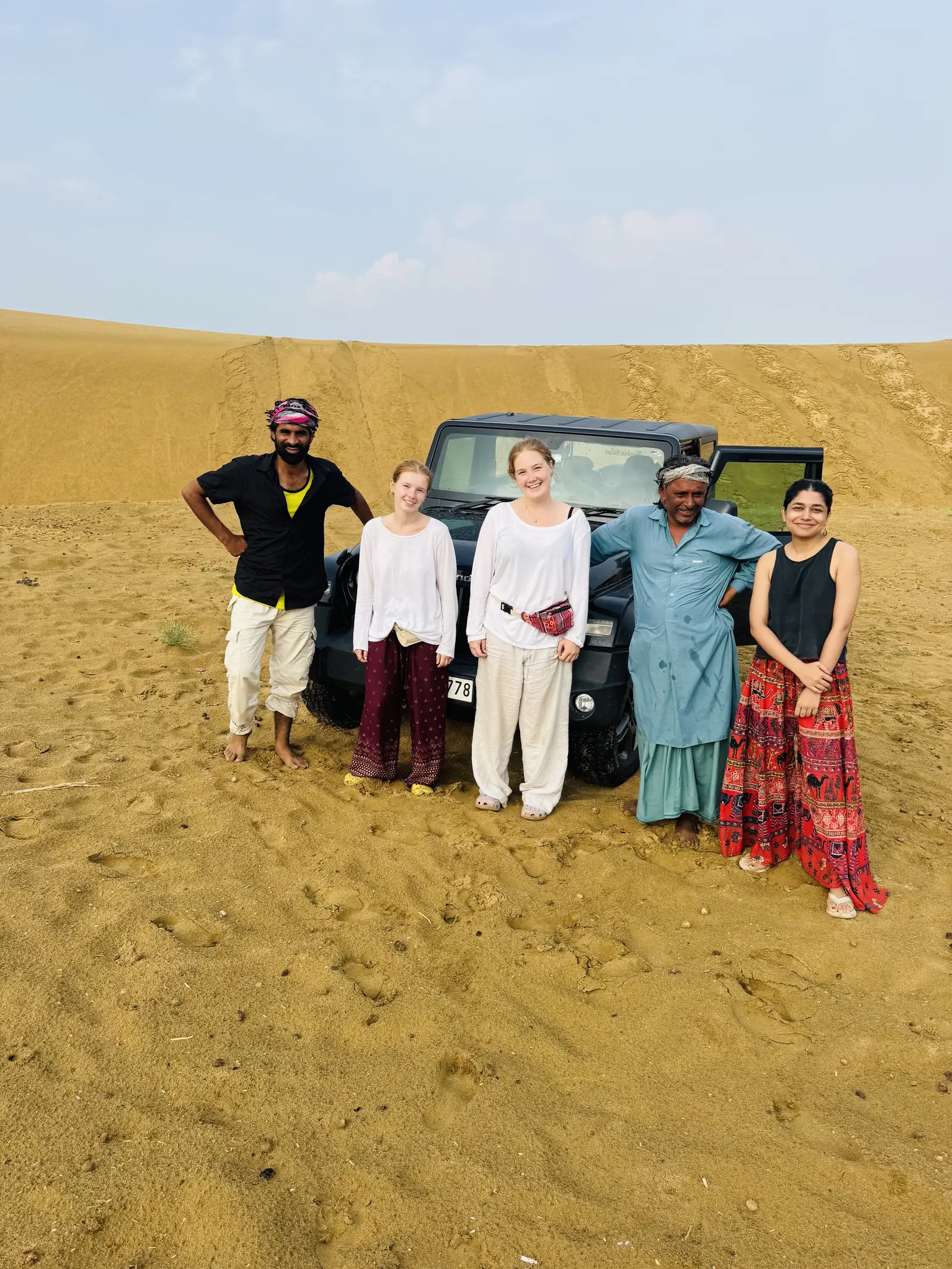 A group standing with their driver in front of the jeep on the sand