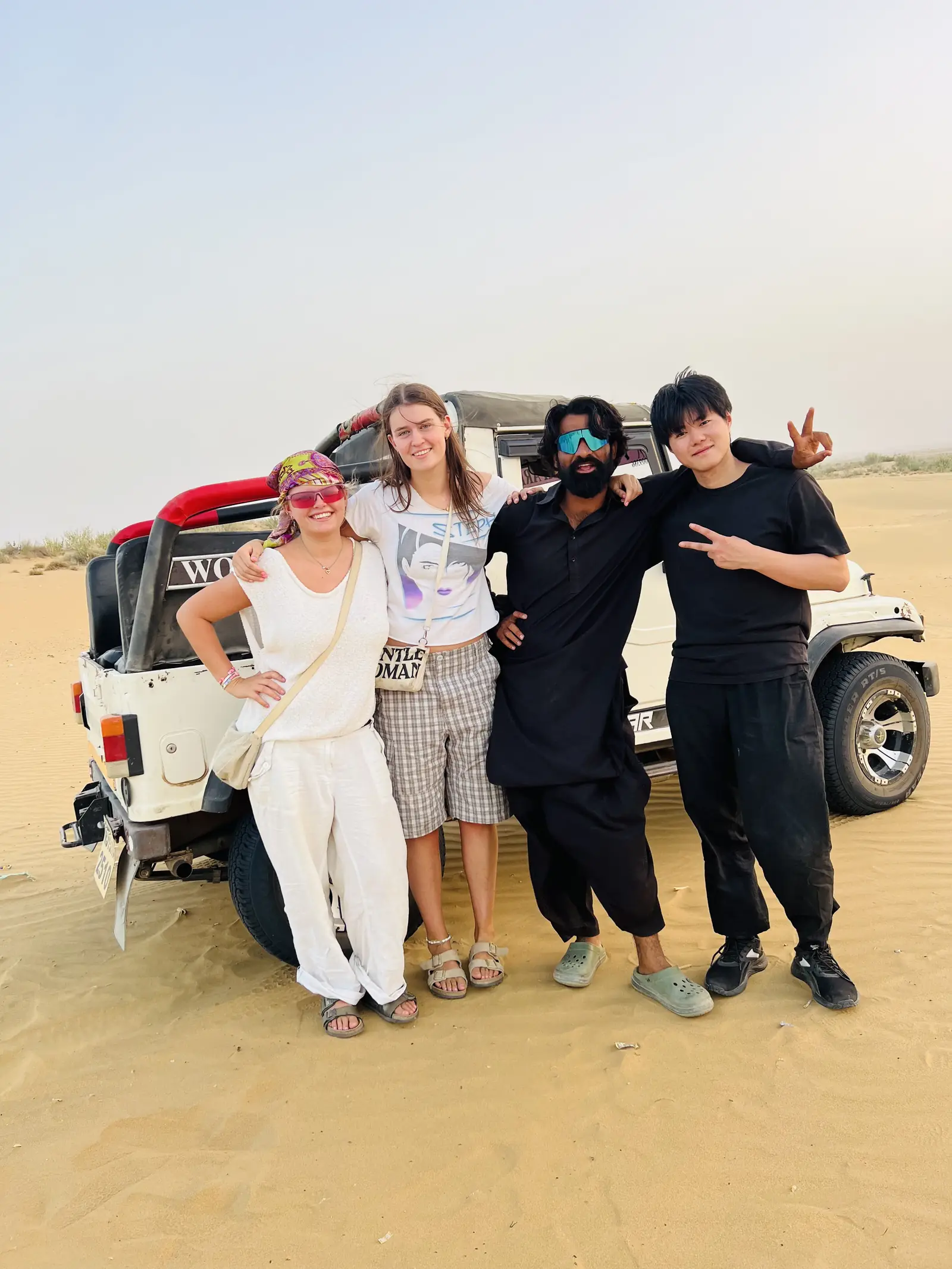 Guests and their guide leaning on the back of the jeep out in the desert