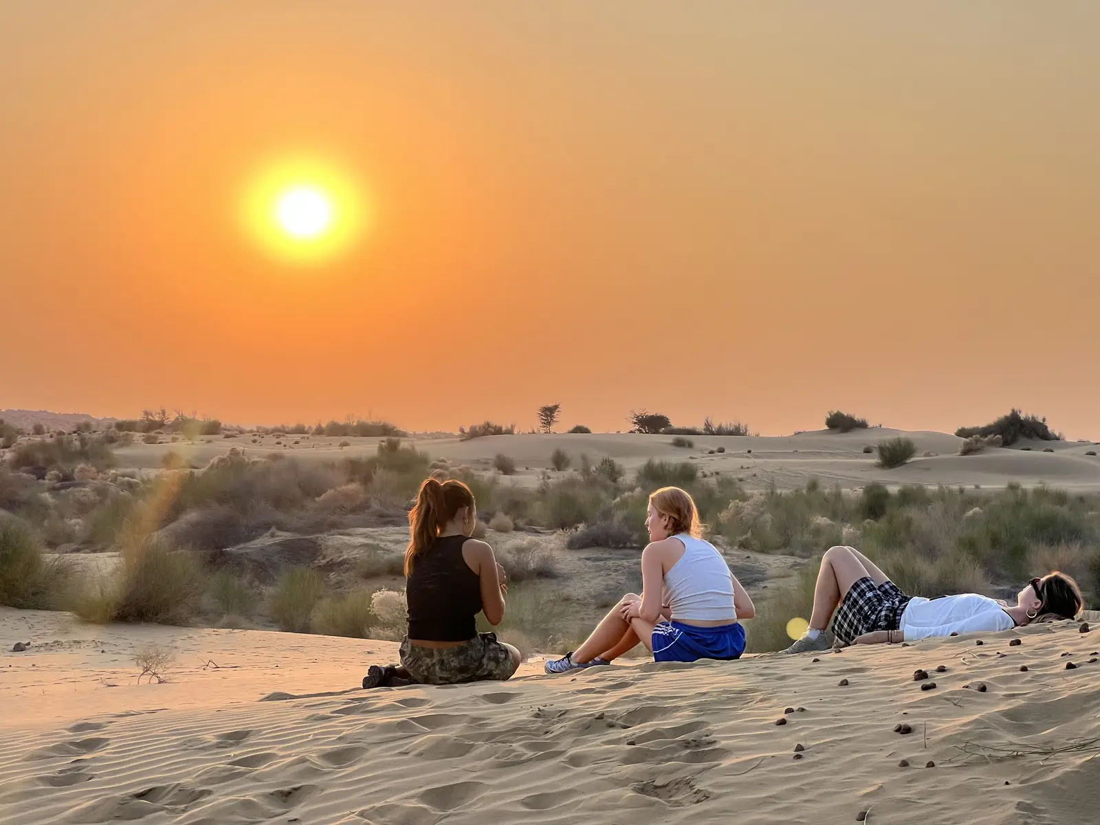 Guests sitting and lying on the sand as the sun drops towards the horizon