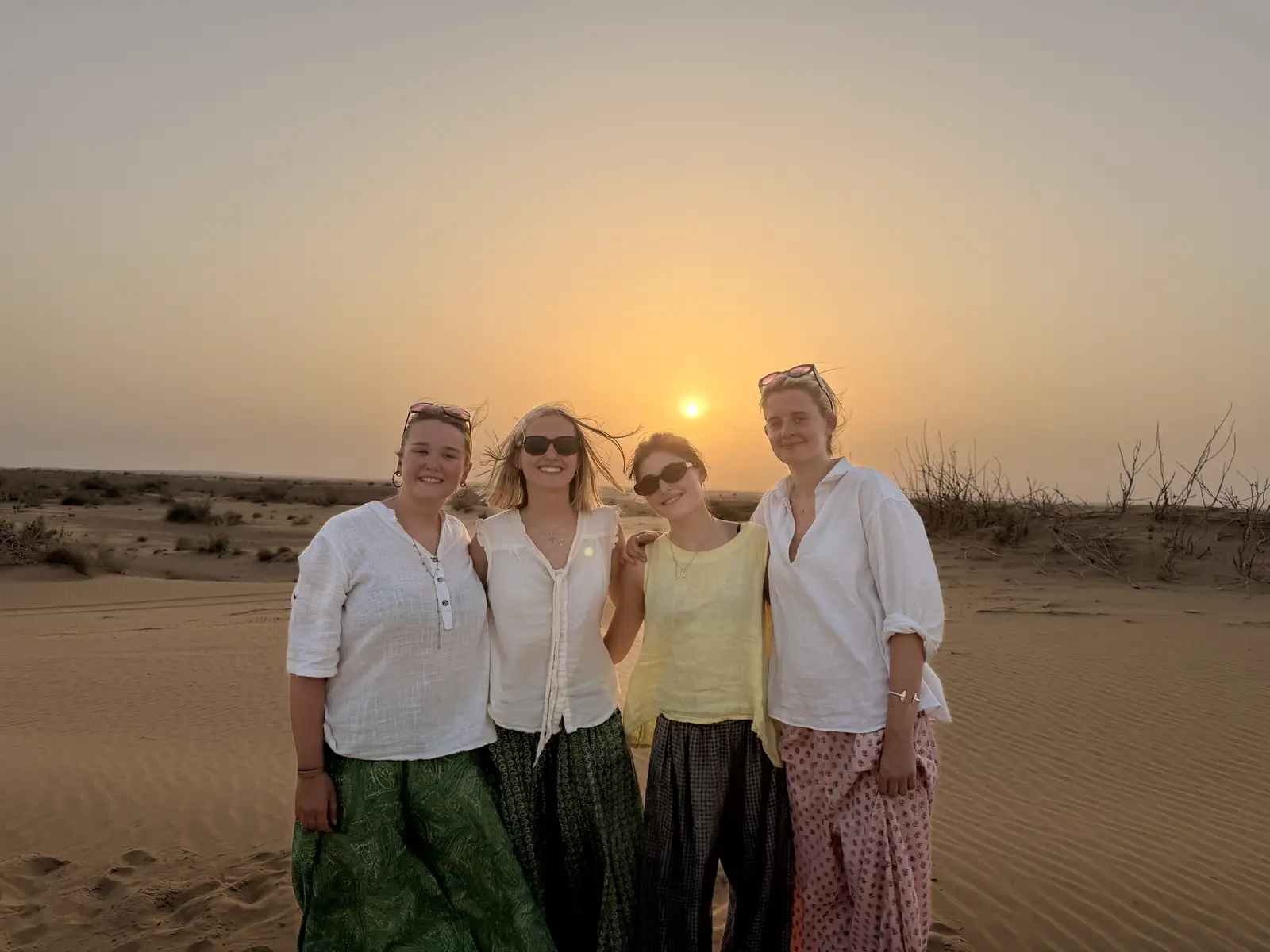 Four guests standing together on the sand at sunset