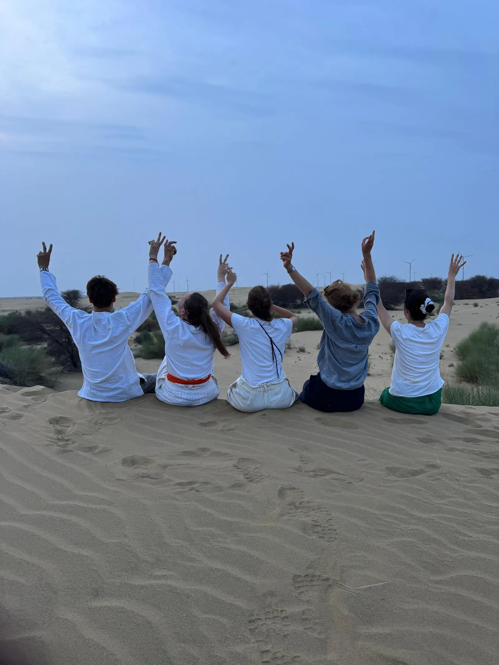 A group sitting on the dune with their arms up, watching the light go