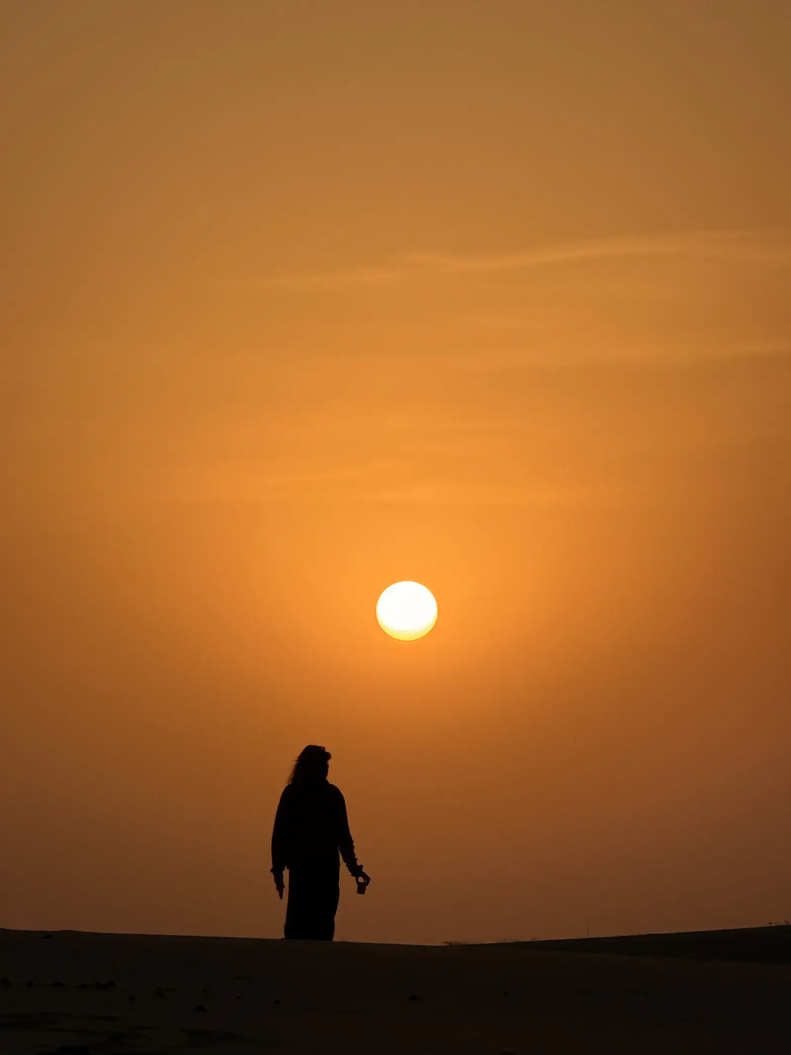 One person on the crest of a dune, silhouetted against a low orange sun
