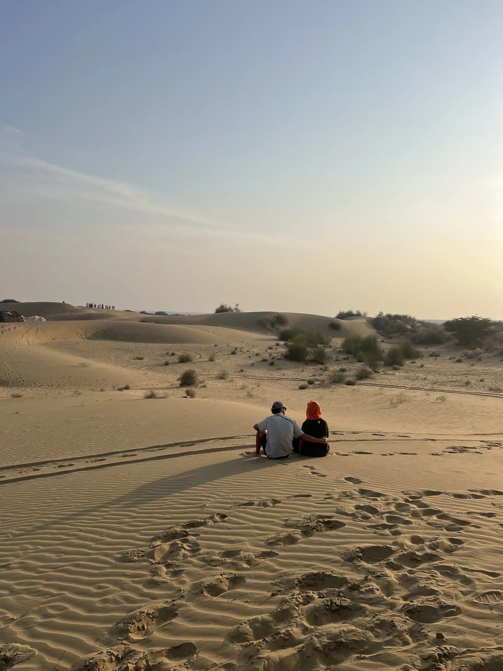 Two guests sitting on the sand at last light, the dunes running away behind them