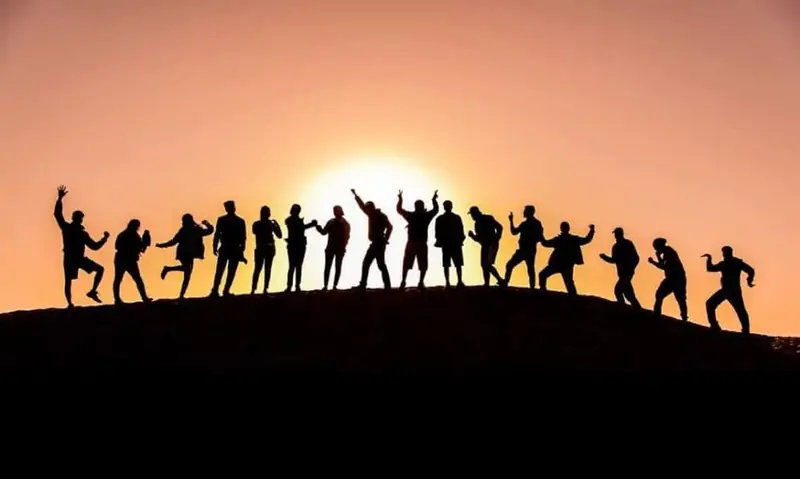 A dozen people silhouetted along a dune ridge against a red sky