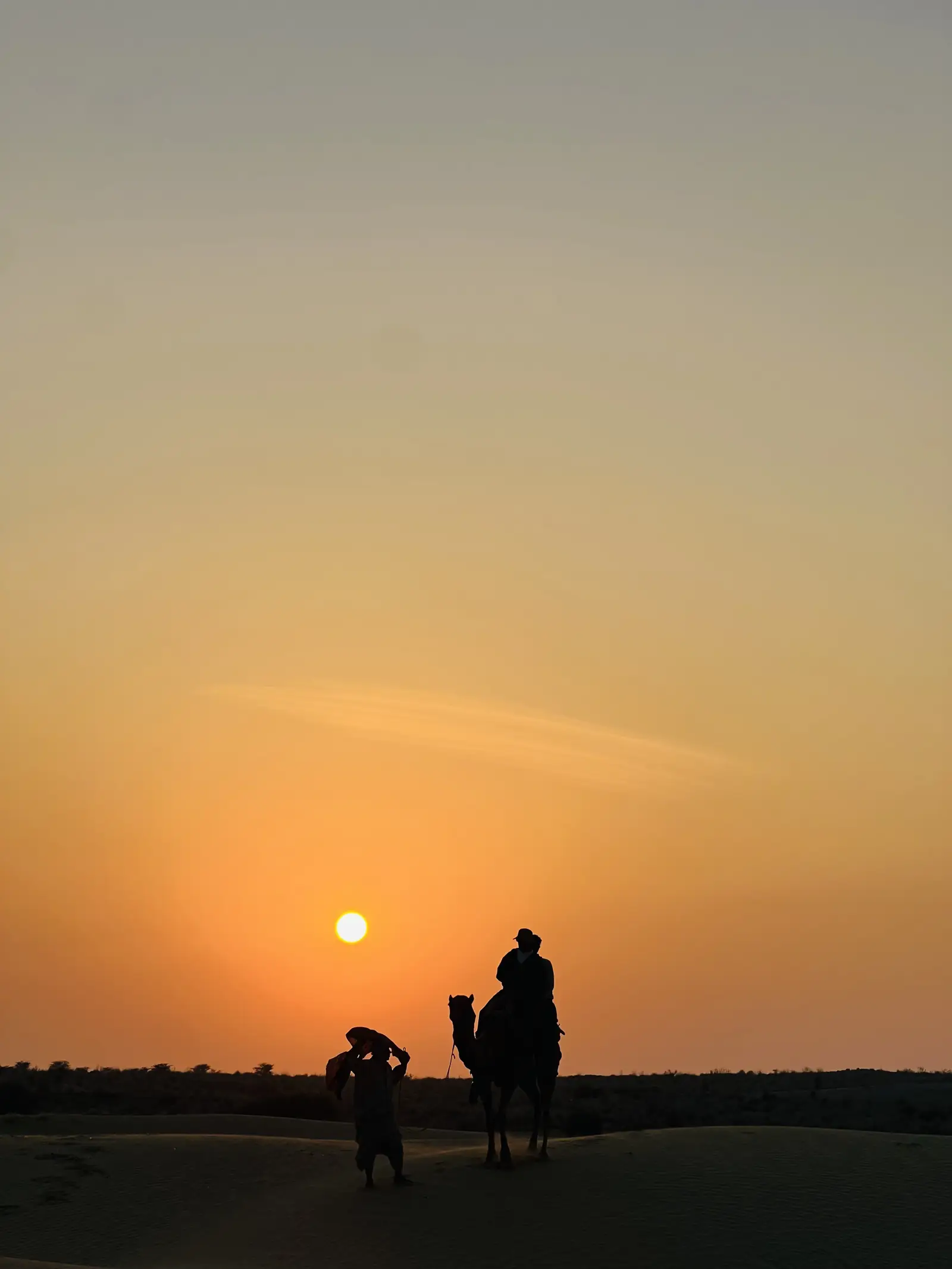 A camel and its guide walking out across the sand at dusk