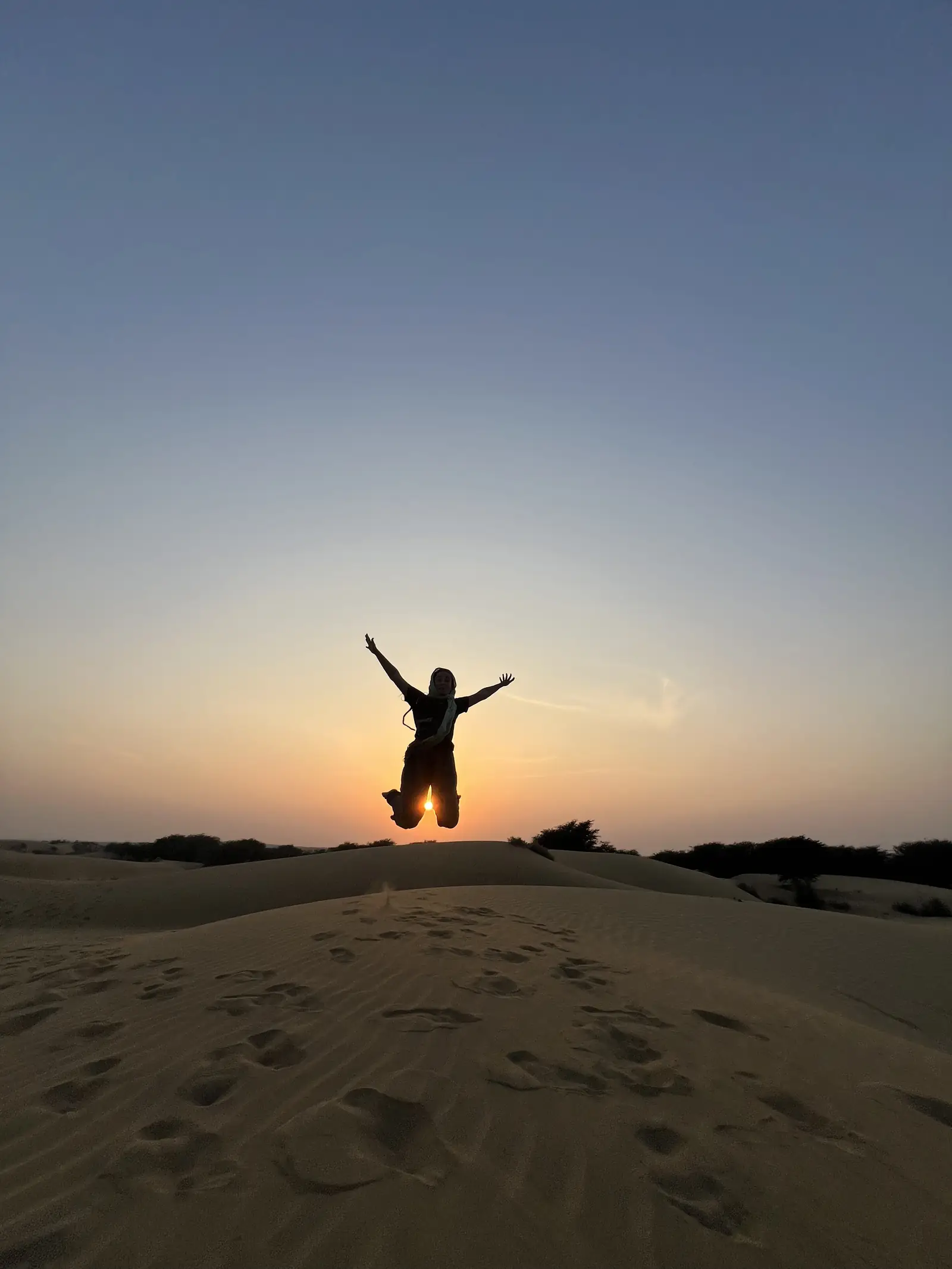 A guest mid-jump, silhouetted against the sun over the dunes