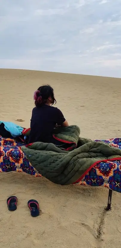A bed made up on the open sand at dawn, slippers beside it