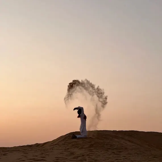 A guest throwing an arc of sand overhead on a dune ridge at dusk