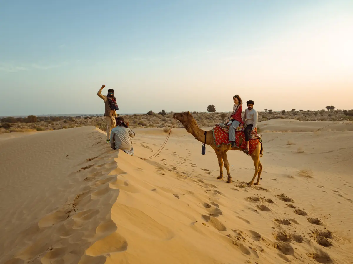 Guests riding camels up the face of a dune in the afternoon