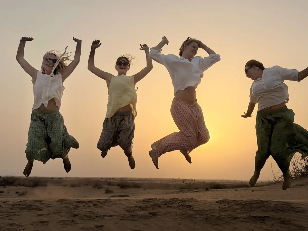 Four guests jumping together on the sand in the golden hour
