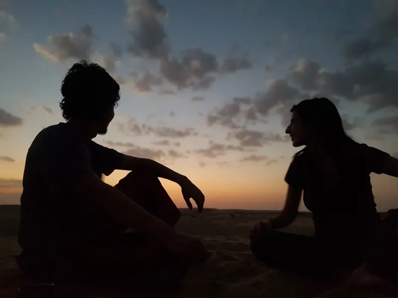 Two guests silhouetted against the sky on a dune at dusk