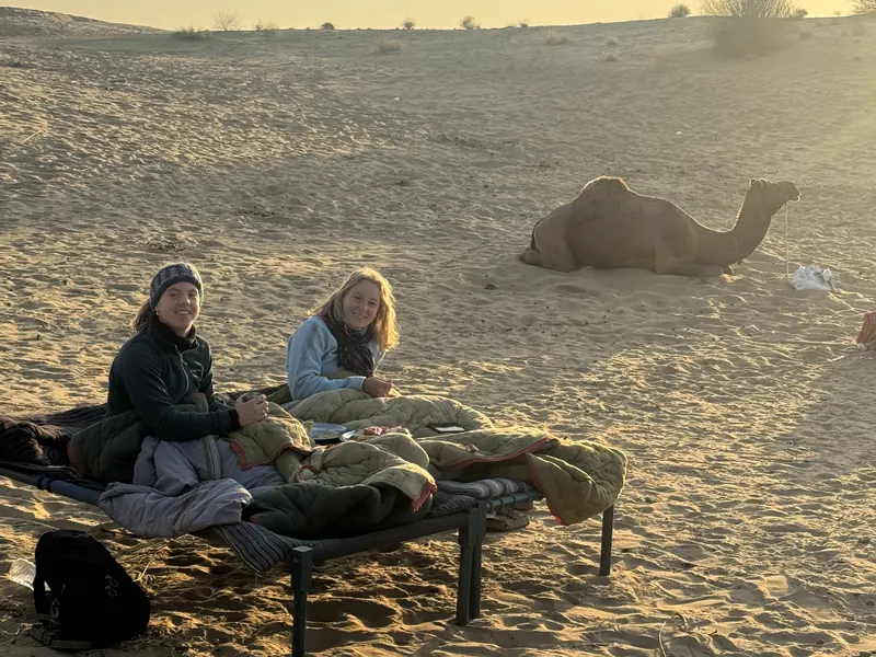 A charpoy bed made up on the open sand at Siala with a camel resting behind it